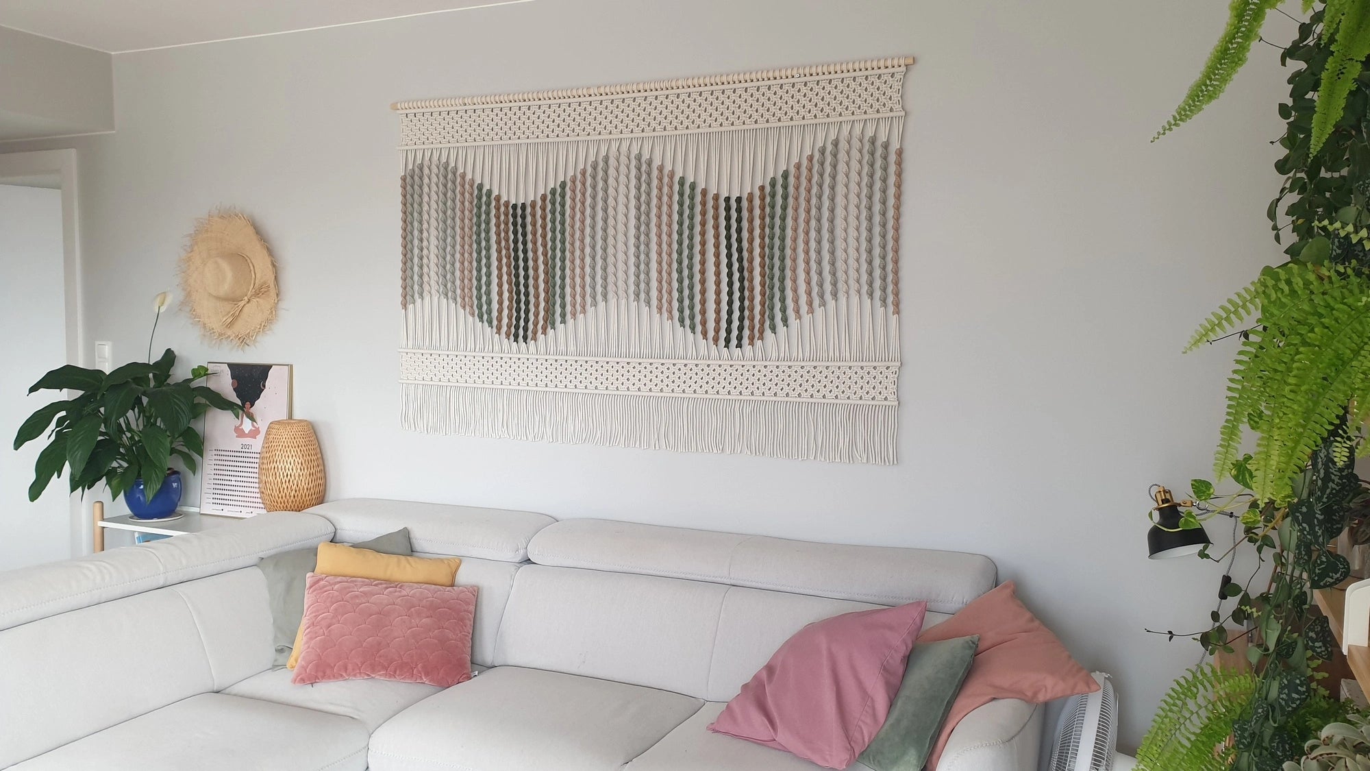 Duża makrama ścienna NORDART w jasnym, nowoczesnym salonie. Ręcznie wykonana dekoracja z naturalnego sznurka zawieszona na ścianie nad sofą, tworząca przytulny, minimalistyczny klimat wnętrza inspirowanego stylem boho i nowoczesnym designem.
