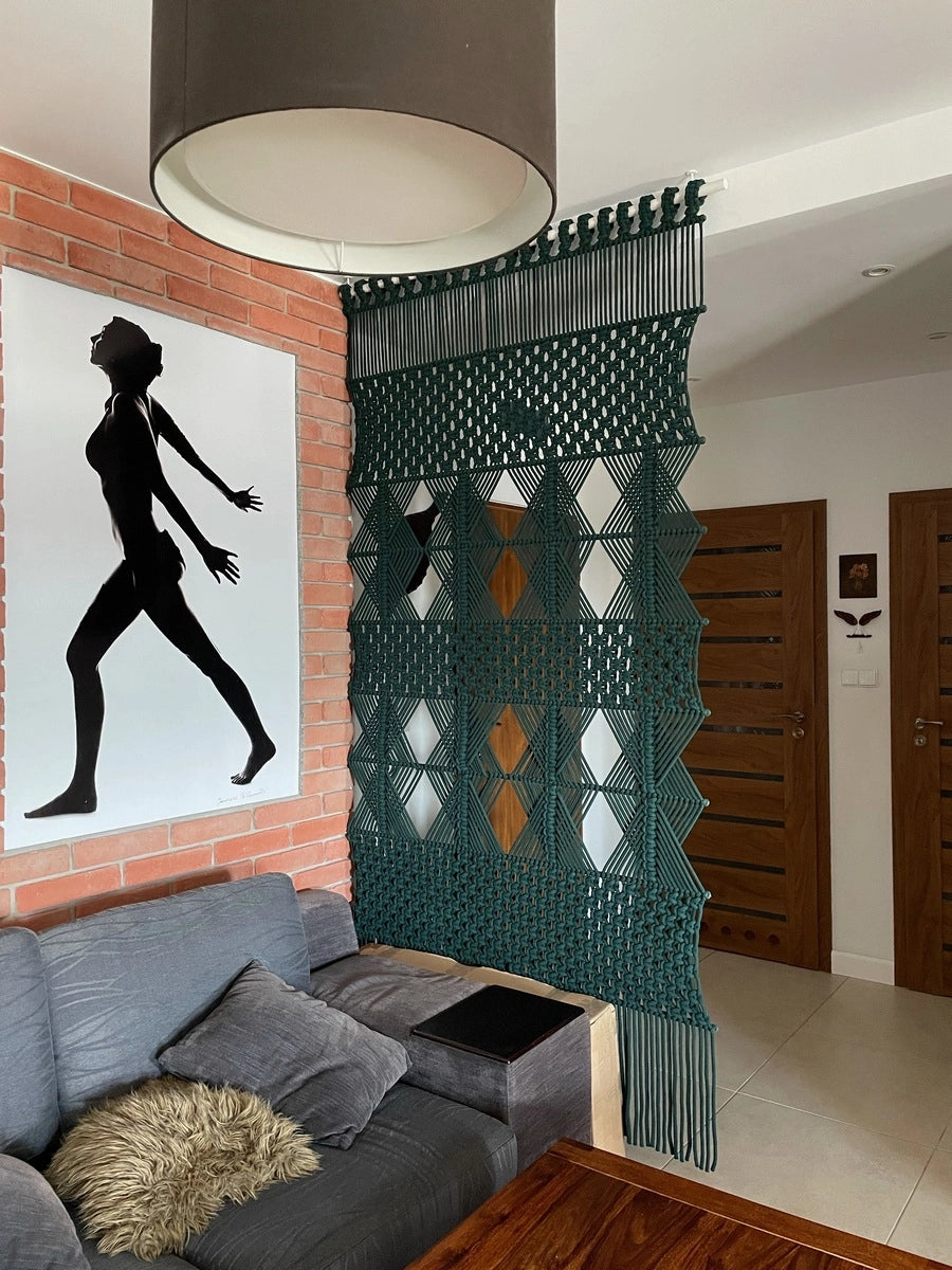 Nowoczesna, geometryczna makrama SKADI w głębokiej butelkowej zieleni, stworzona na zamówienie jako funkcjonalna ścianka działowa między korytarzem a salonem. Duża, autorska dekoracja NORDART łączy minimalistyczny design z praktycznym podziałem przestrzeni.