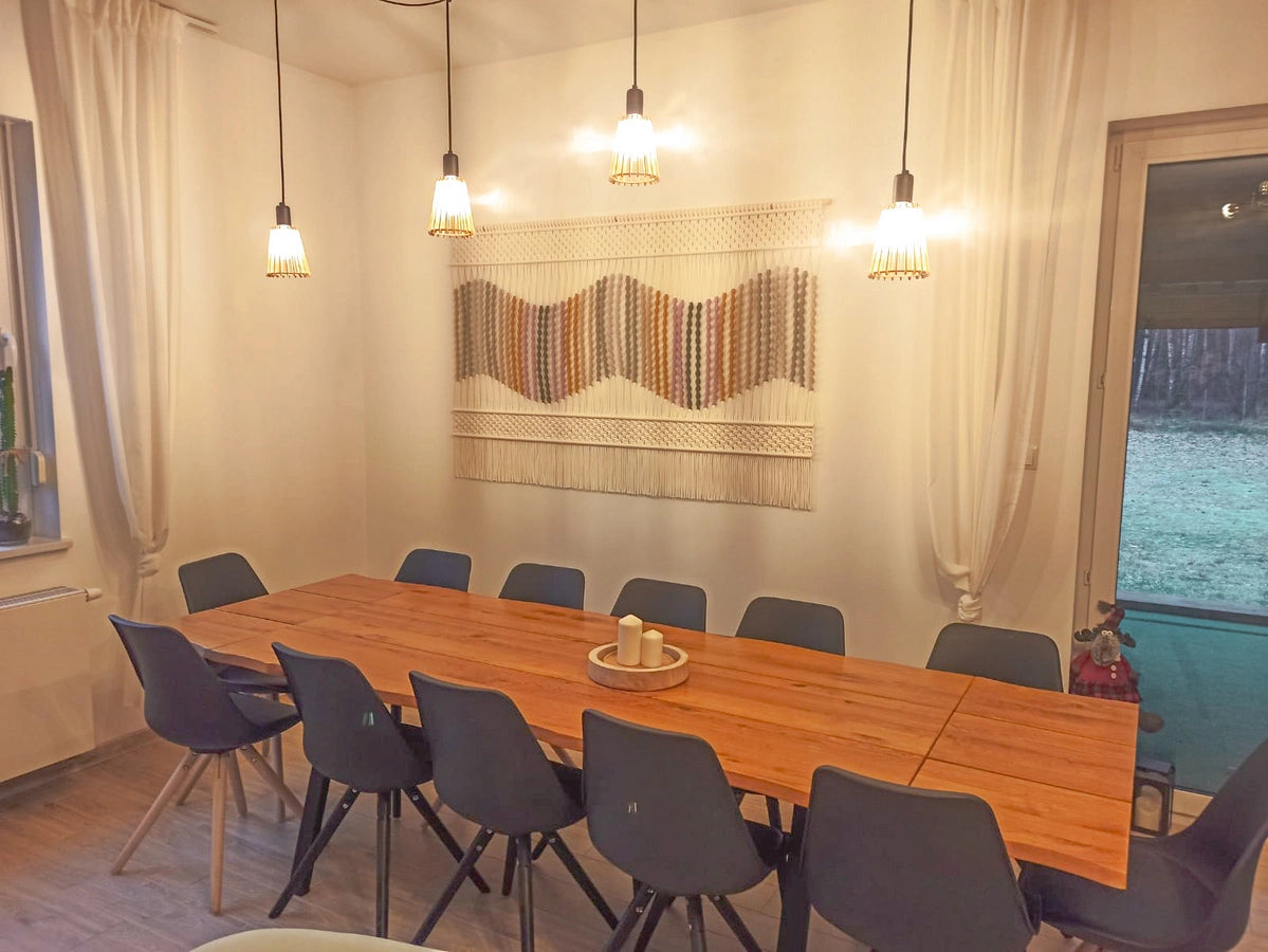 Przytulna jadalnia z dekoracją ścienną w formie makramy NORDART „Seaside Dunes”. Ręcznie wykonana makrama w kolorze ecru z falistym wzorem w odcieniach beżu i zieleni, zawieszona nad stołem w części jadalnianej salonu.