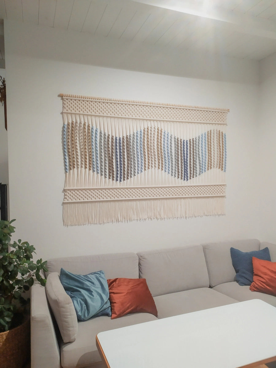 Przytulny salon z ręcznie wykonaną makramą NORDART jako dekoracją ścienną. Duża makrama w naturalnej kolorystyce zawieszona nad kanapą, podkreślająca harmonijny i spójny charakter wnętrza.